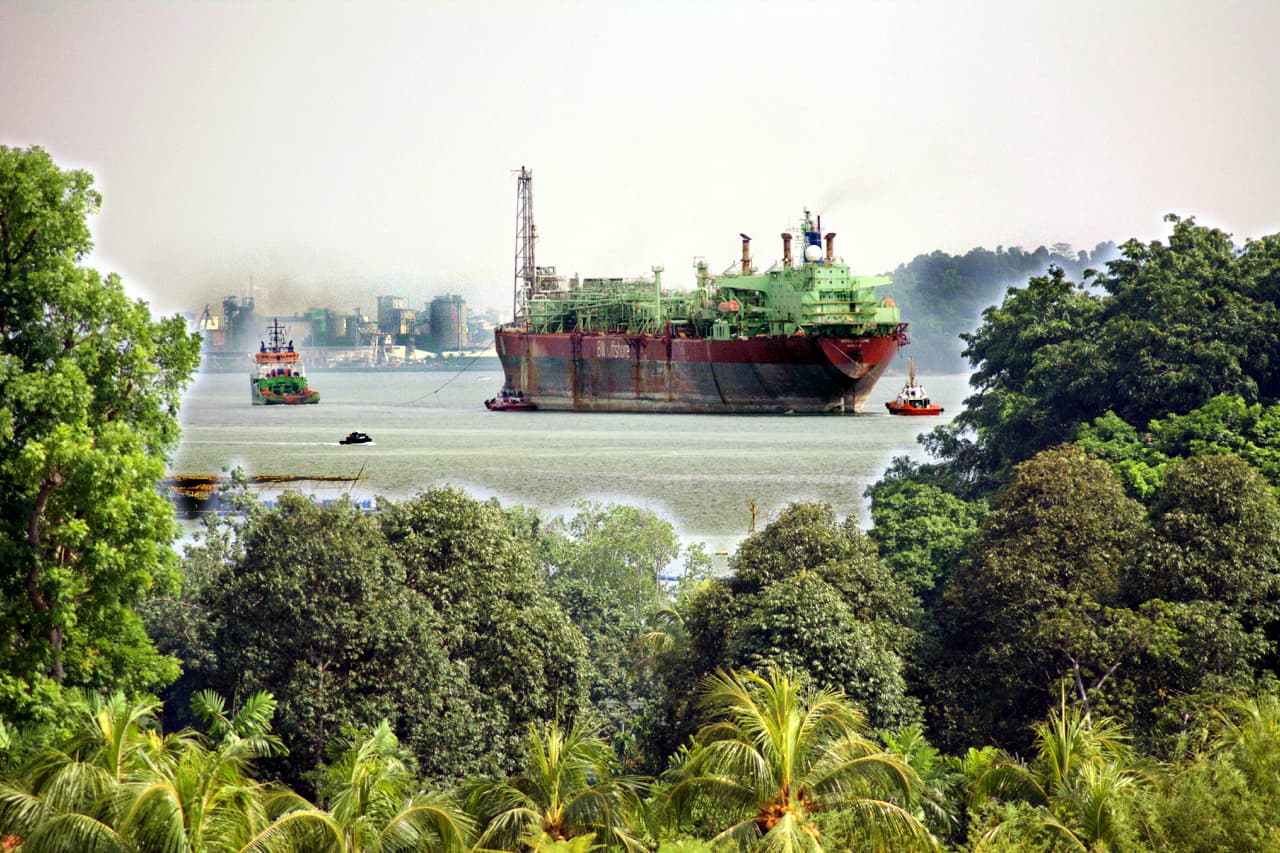 A large oil tanker being assisted by smaller boats in a harbor area.