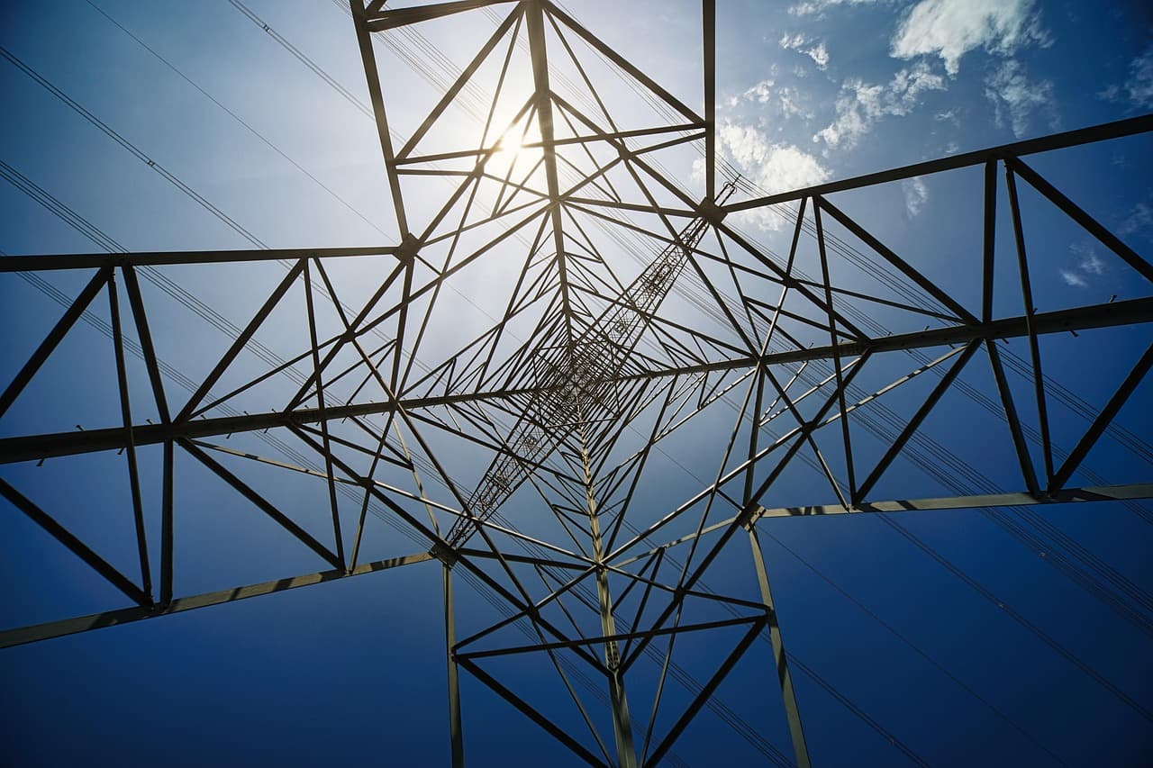 A high-voltage power line tower against a blue sky.