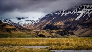 Isländskt landskap med berg och gräsmark under en molnig himmel.