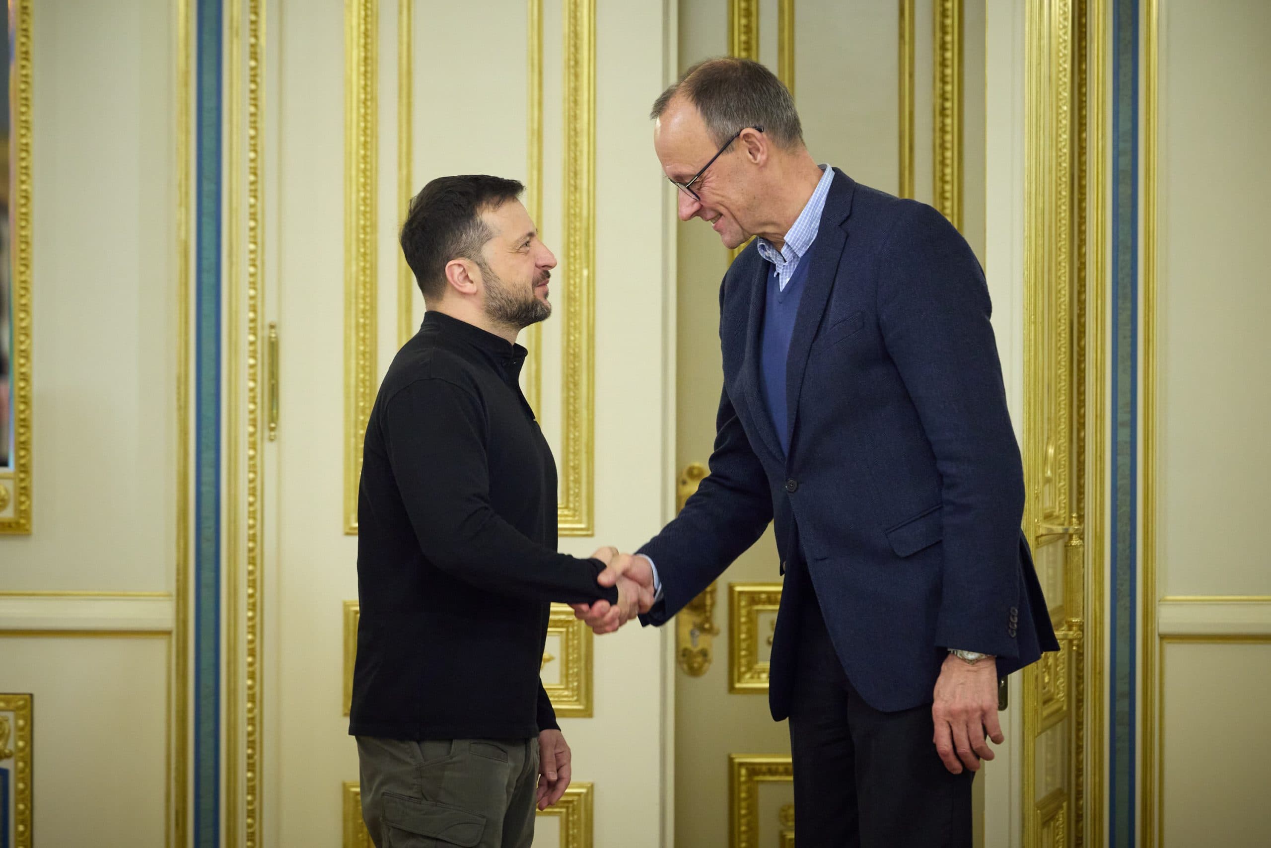 Volodymyr Zelenskyy and Friedrich Merz shaking hands in a formal setting.