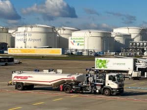 Reklam för Sustainable Aviation Fuel på Frankfurts flygplats med bränsletankar i bakgrunden.