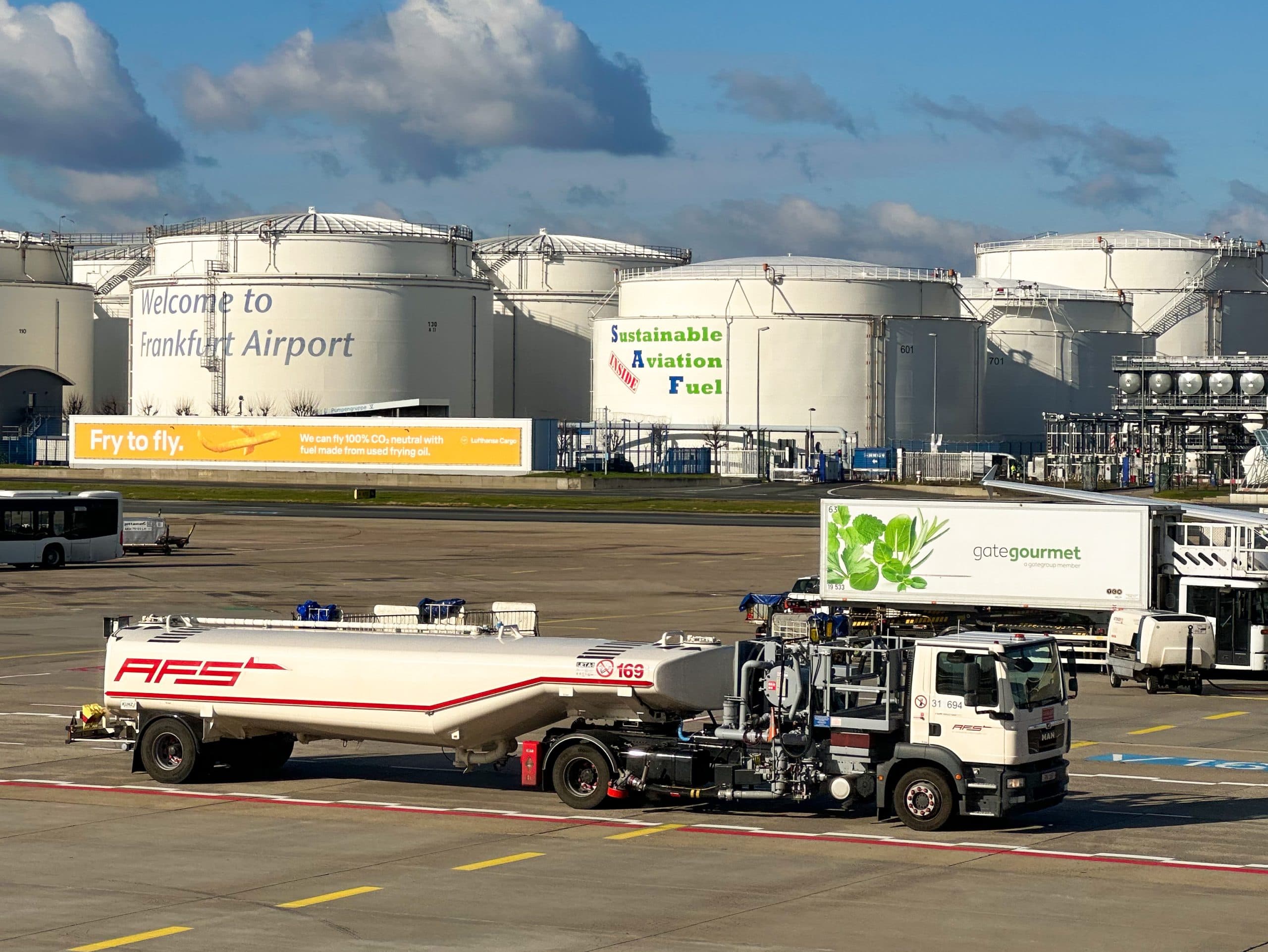 Sustainable Aviation Fuel advertisement at Frankfurt Airport with fuel tanks in the background.