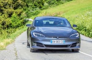En svart Tesla Model S kör på en väg omgiven av grönska.
