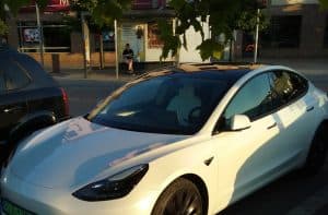 En vit Tesla Model 3 parkerad på en gata med träd i bakgrunden.