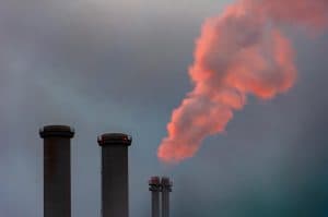 Rök som stiger från industriskorstenar mot en molnig himmel.