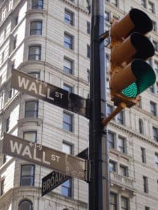 Wall Street-gatuskylt med trafikljus och byggnader i bakgrunden.