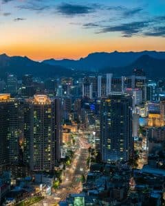 Vy över Seoul med skyskrapor och berg i bakgrunden vid solnedgången.