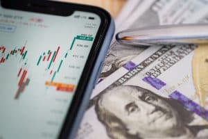 Smartphone som visar börsdata bredvid amerikanska dollarsedlar.