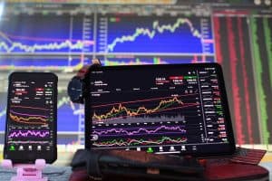 En smartphone och en surfplatta visar aktiekurser och grafer framför en stor skärm med börsdata.