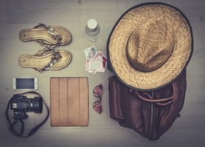 Ovanifrån-arrangemang av semesterprylar, däribland en hatt, sandaler, kamera och ryggsäck.