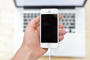 Hand som håller en iPhone med en laddkabel ansluten.
