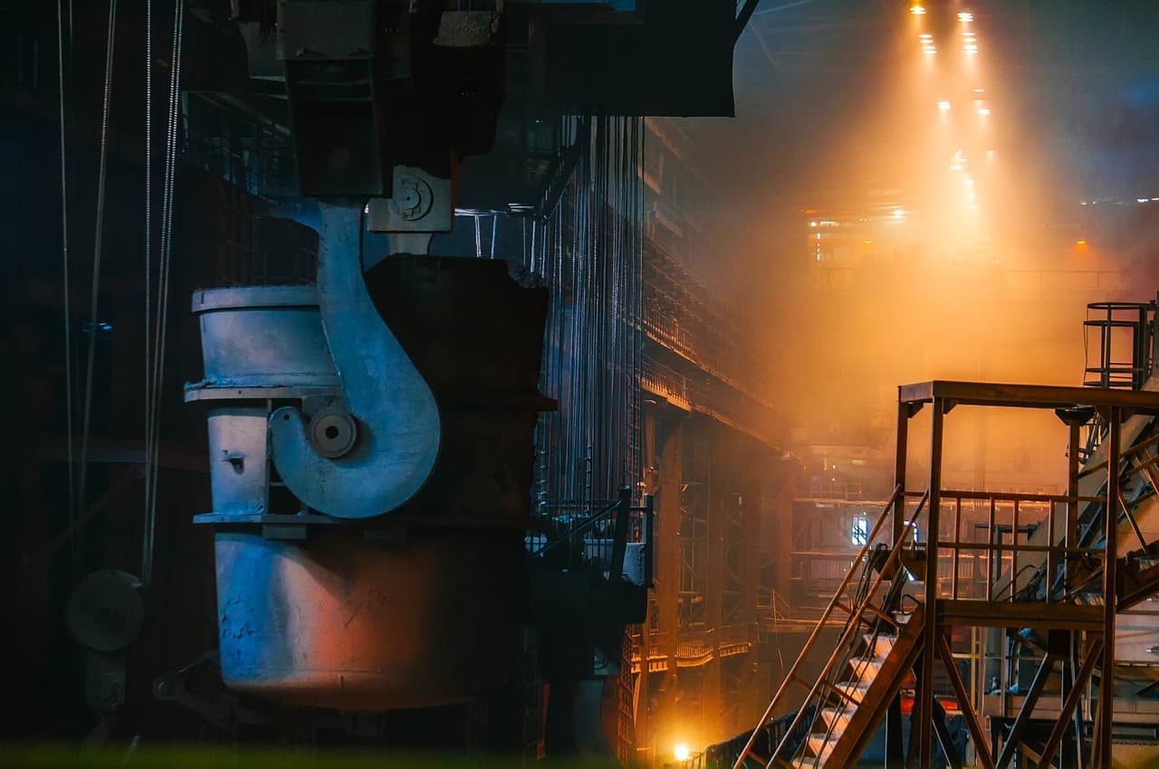 Interior of a steel factory with machinery and orange lighting.