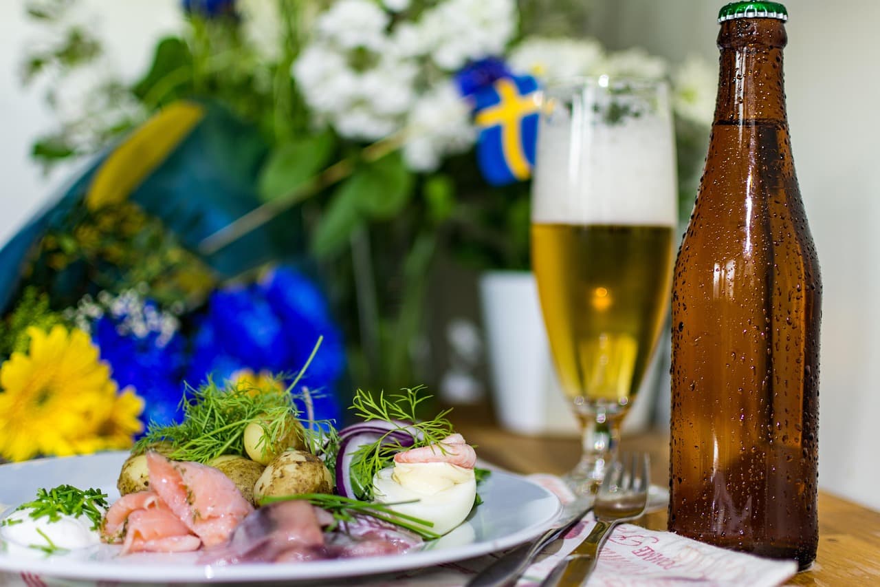 Tallrik med traditionell svensk midsommarmat och en ölflaska.