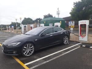 En svart Tesla bil laddas vid en laddstation.