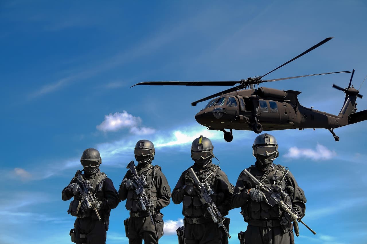 Fyra soldater i militäruniform framför en helikopter mot en blå himmel.