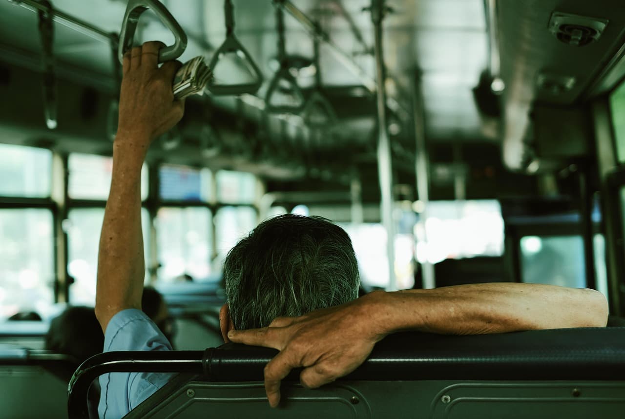 En man sitter på en buss och håller i ett handtag.