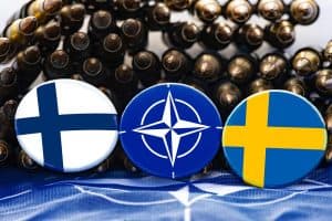 Nato-emblem med finska och svenska flaggor på knappar omgivna av patroner.
