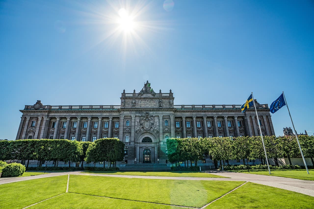 Sveriges riksdag med svenska och EU-flaggor i förgrunden.
