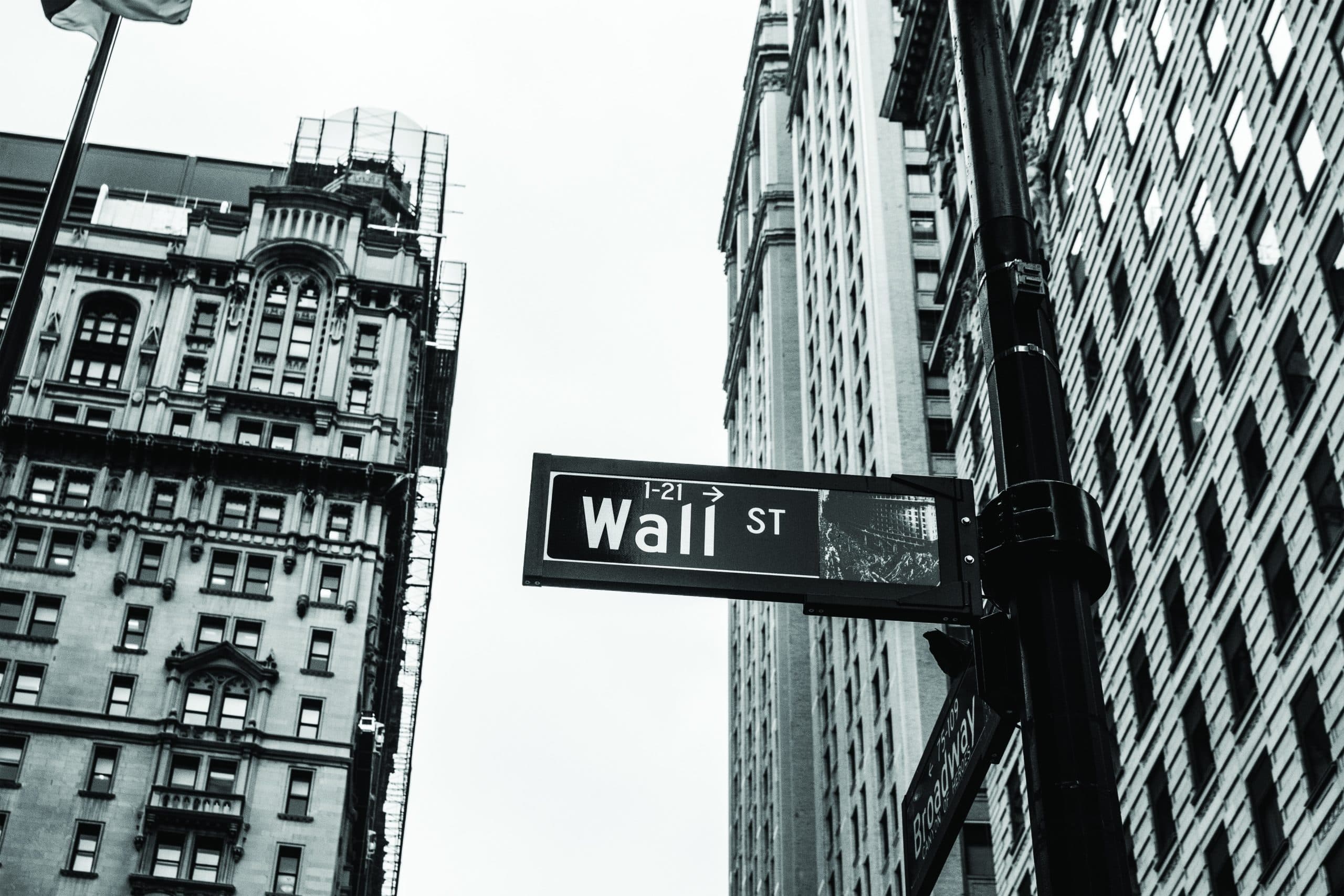 Monochrome image of a Wall Street sign with buildings in the background.