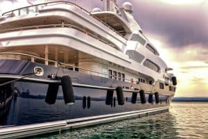 En lyxig yacht förtöjd i lugnt vatten med en solnedgång i bakgrunden.