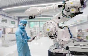 En tekniker i skyddskläder arbetar med en stor robotarm i en industriell miljö.