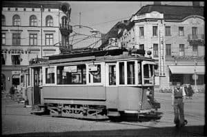 En äldre spårvagn på en gata i Uppsala med historiska byggnader i bakgrunden.