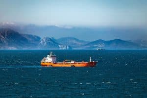 En orange oljetanker seglar på havet med berg i bakgrunden.