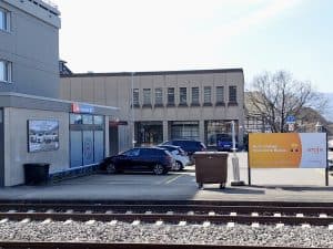 En byggnad med en Bahnhof-skylt och parkerade bilar framför.