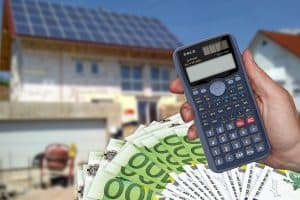 En hand håller en miniräknare och euro-sedlar framför ett hus under konstruktion.