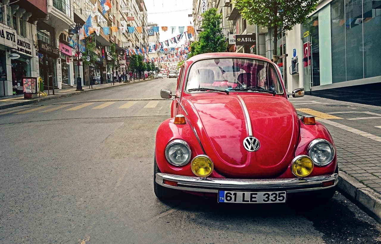 En röd Volkswagen Beetle parkerad på en tom gata med flaggor ovanför.