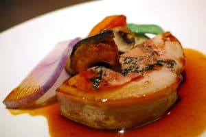 En tallrik med foie gras och grönsaker i en sås.