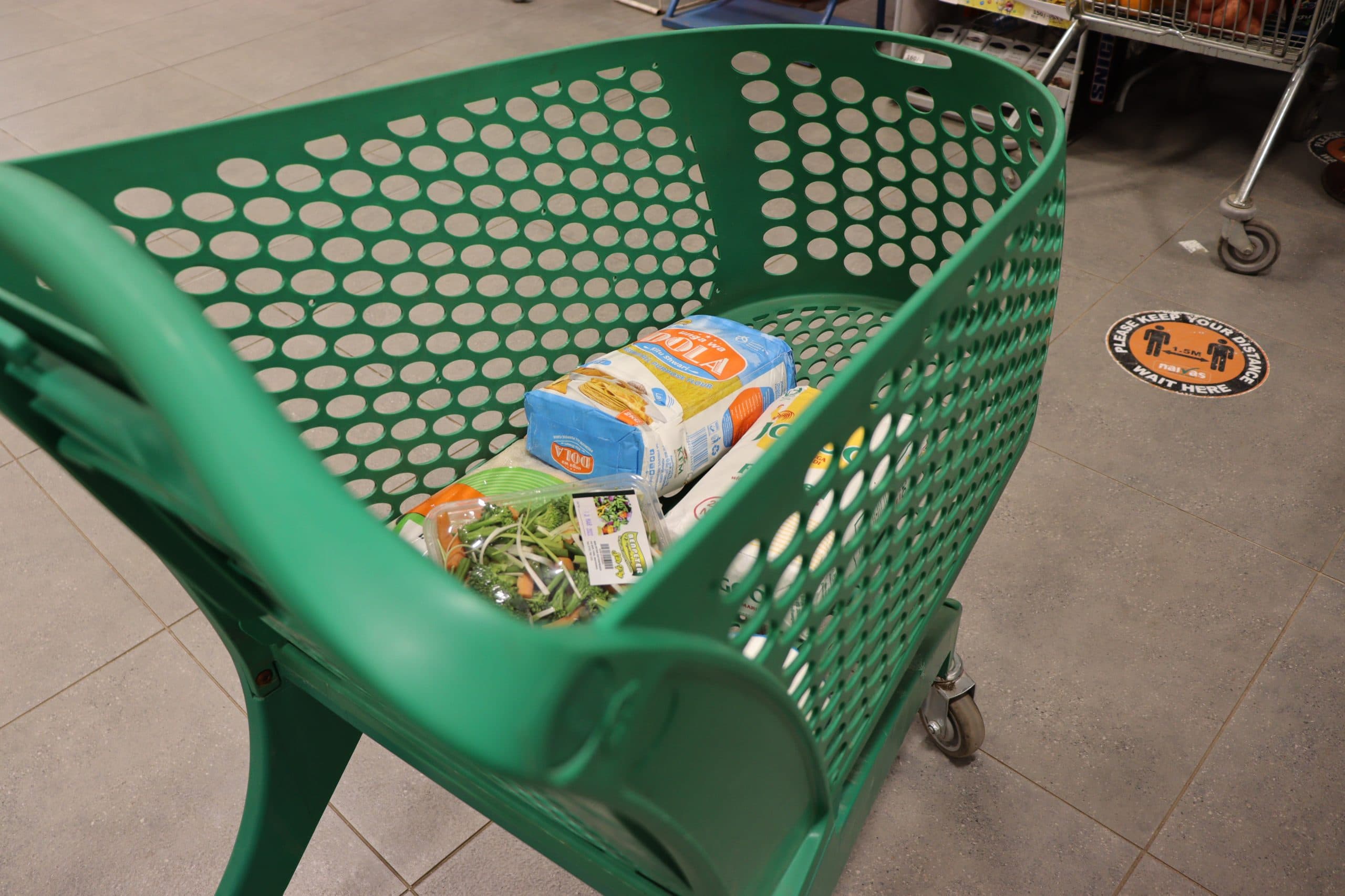 A green shopping cart with groceries inside a supermarket.