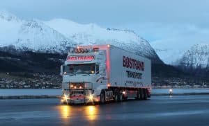En stor lastbil med texten 'Bostrands Transport' på en väg med berg i bakgrunden.