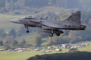 Ett Gripen-stridsflygplan i luften över ett landskap.