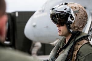 Soldat med hjälm och solglasögon som står nära ett militärflygplan.