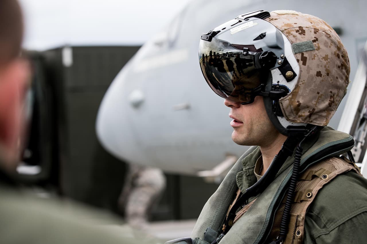 Soldier wearing a helmet and sunglasses standing near a military aircraft.