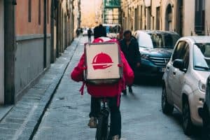 En Foodora-bud cyklar på en gata med en stor leveranslåda på ryggen.