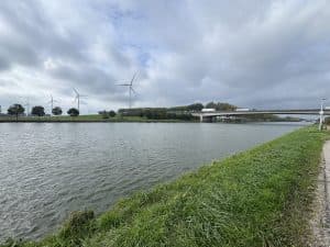Vindkraftverk längs en kanal med en bro i bakgrunden.