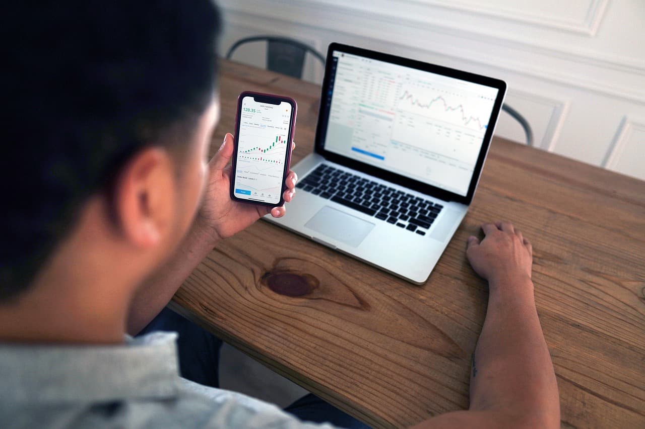 Person som tittar på aktiediagram på en smartphone och laptop.