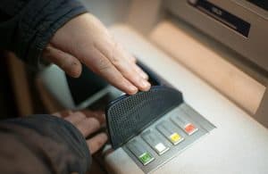 En person skyddar sin PIN-kod vid en bankomat.