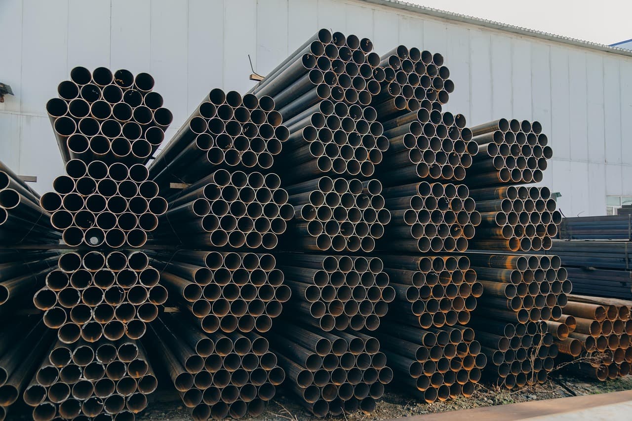 Stapel av stålrör utanför en industribyggnad.
