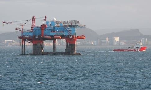 An offshore oil rig in the sea with a ship nearby.