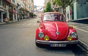 Röd Volkswagen Beetle parkerad på en gata med flaggor ovanför.