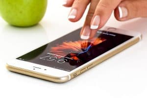 Hand touching a smartphone screen with an apple in the background.