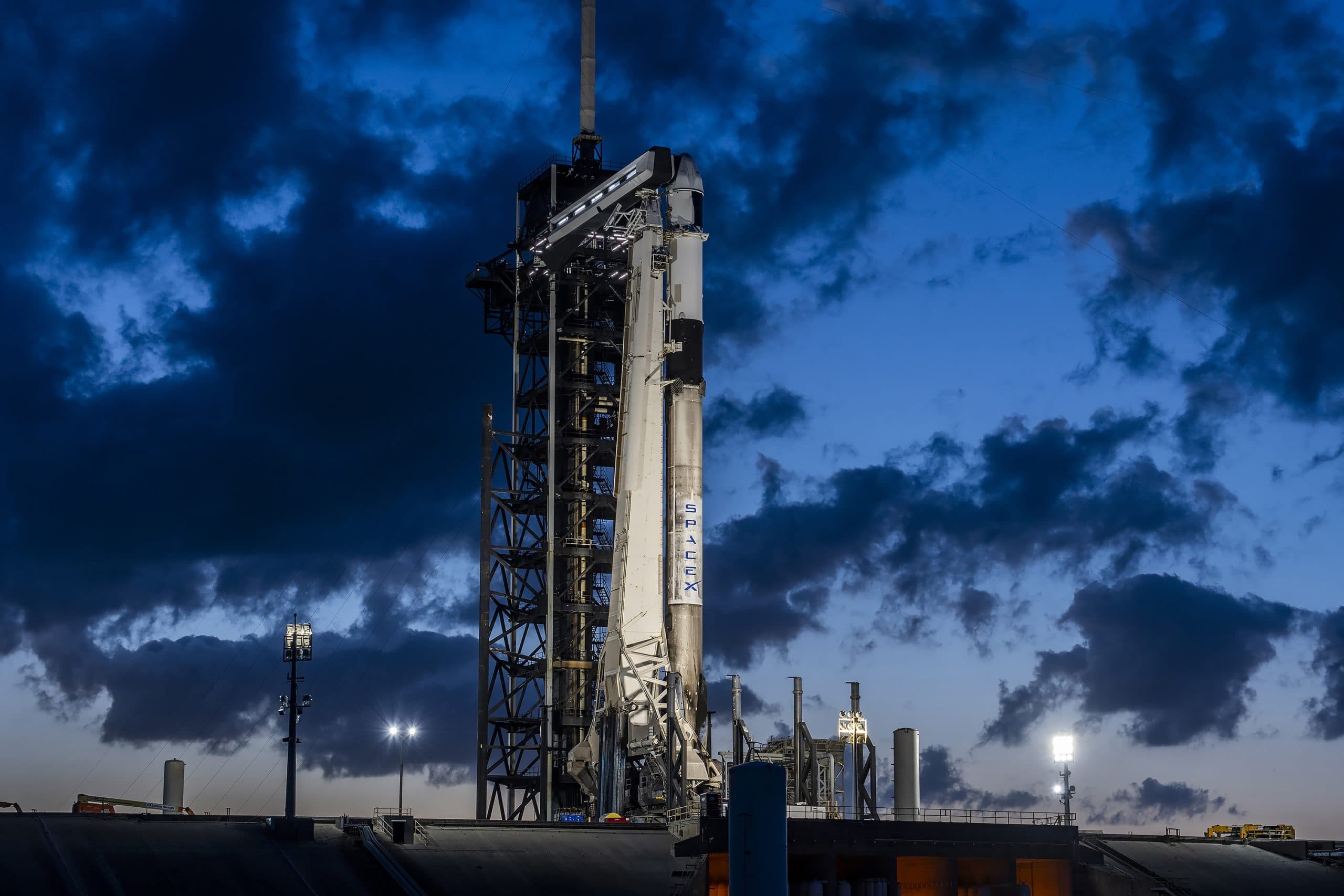SpaceX rocket on launch pad at dusk with dramatic clouds.
