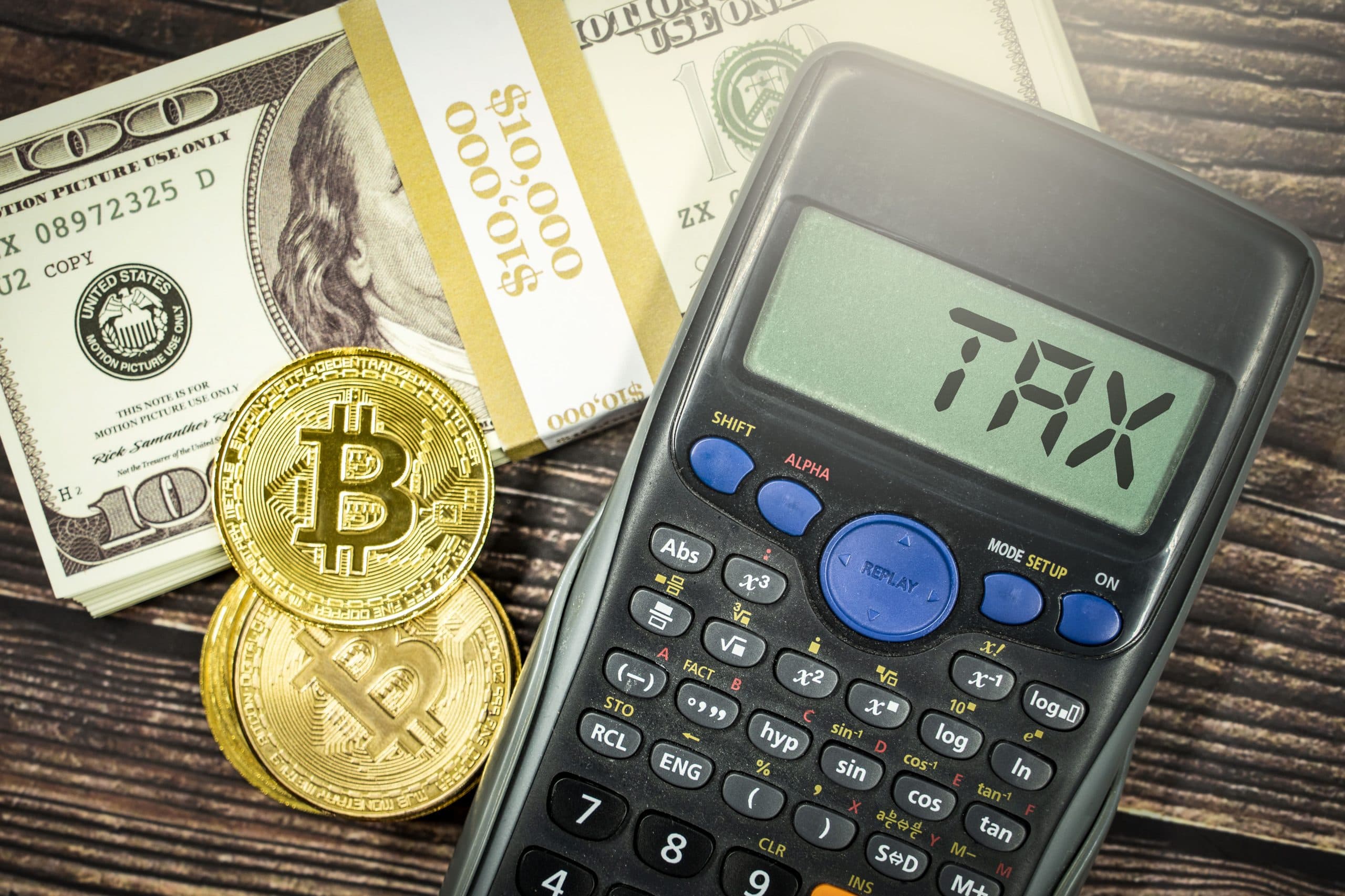 Bitcoinmynt och en miniräknare med texten 'TAX' bredvid amerikanska dollarsedlar.
