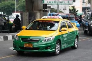 En gul och grön taxi med taxameter på en gata i Bangkok.