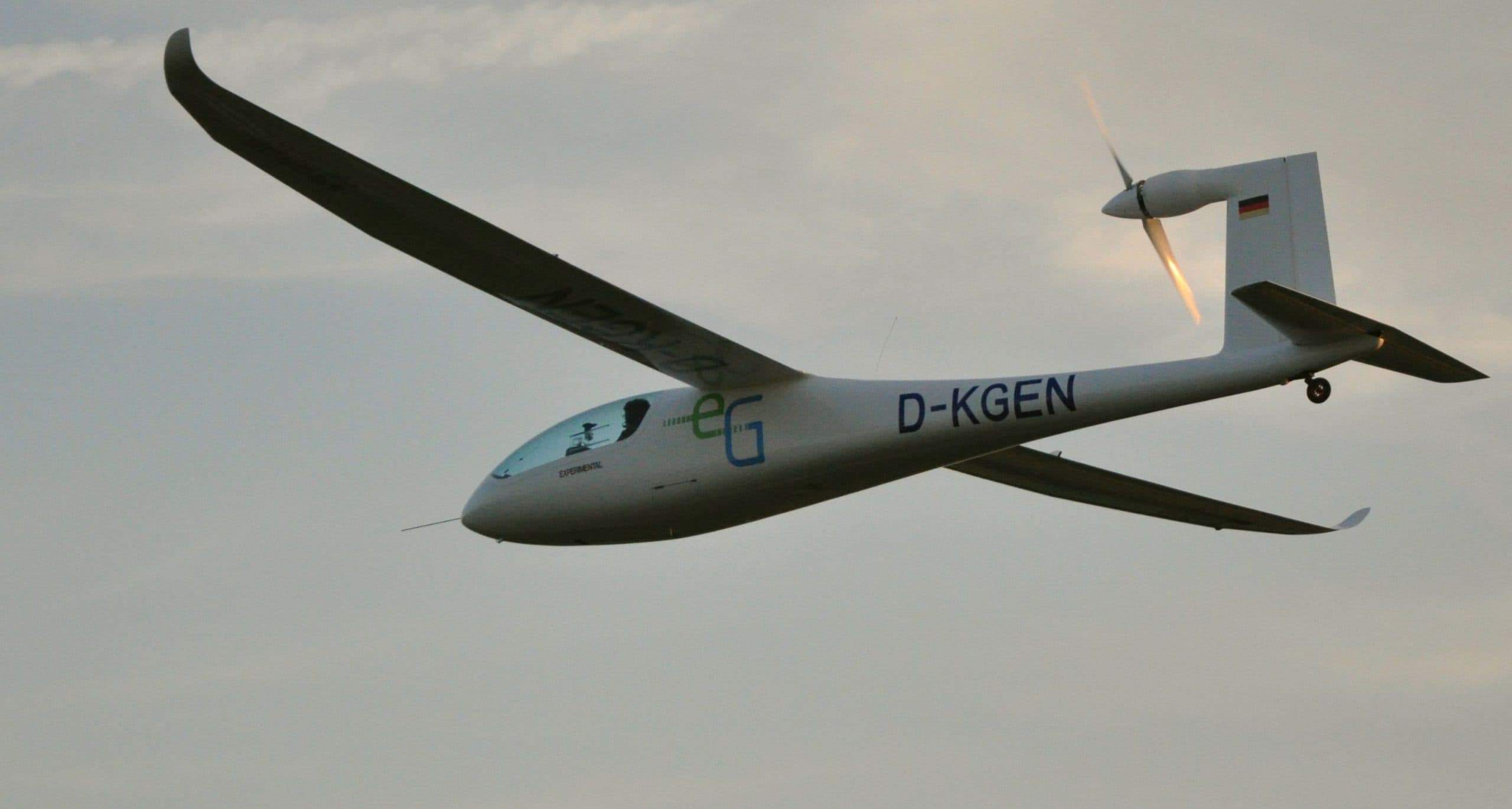 Ett elflygplan i luften mot en molnig himmel.