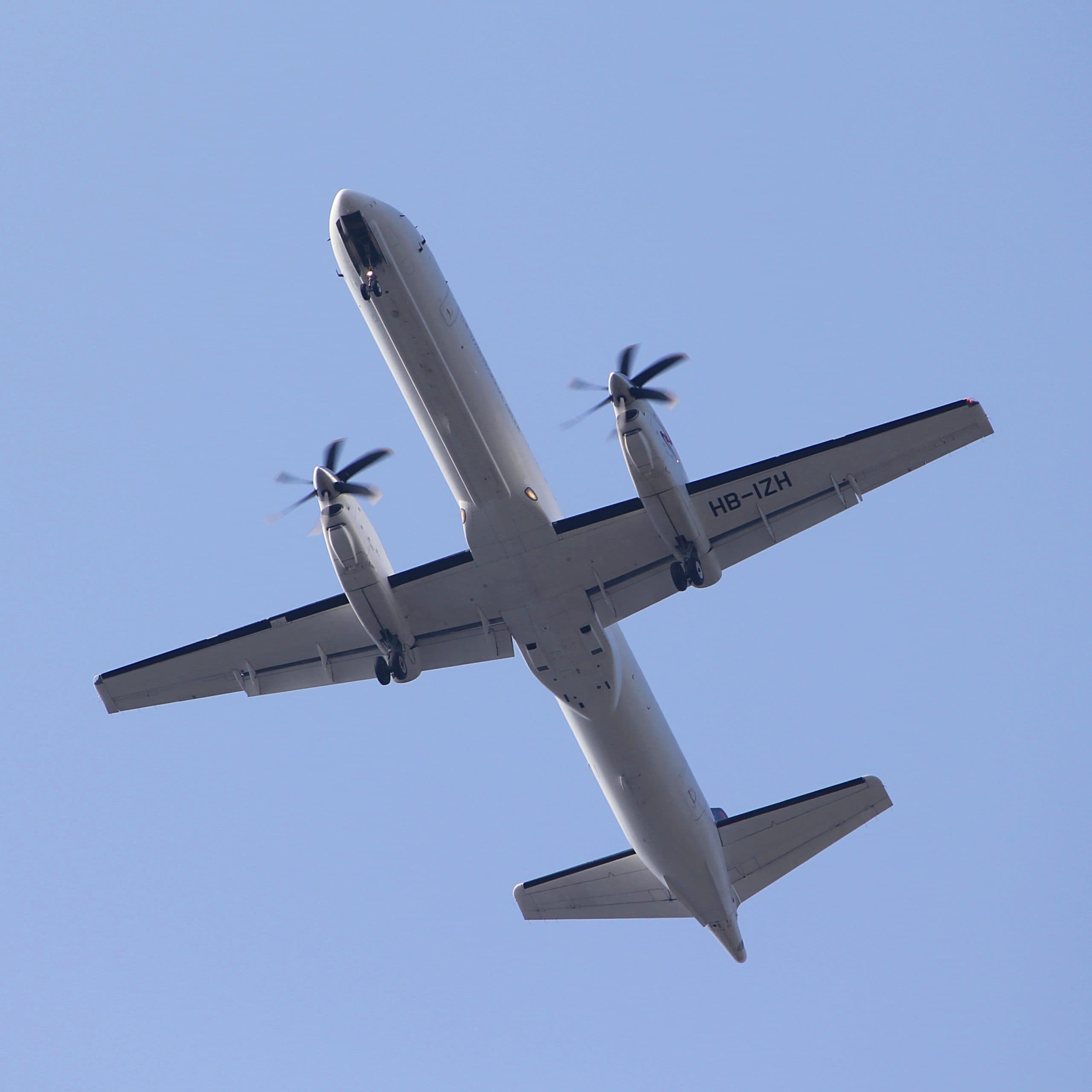 Ett Saab-2000 flygplan fotograferat underifrån mot en klarblå himmel.