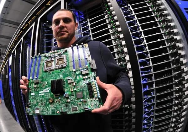 En person håller upp ett serverkort framför en serverrack.